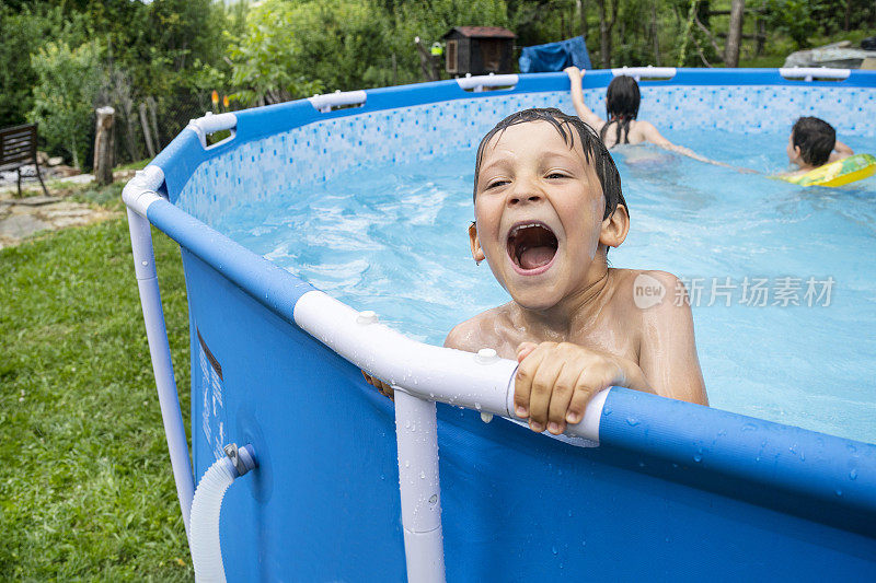 一个小男孩张着嘴笑着，和他的兄弟姐妹们一起抓住游泳池的一侧