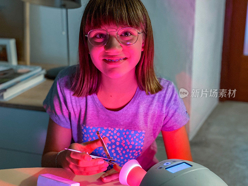 女孩微笑着，用加热灯在塑料手上练习凝胶指甲