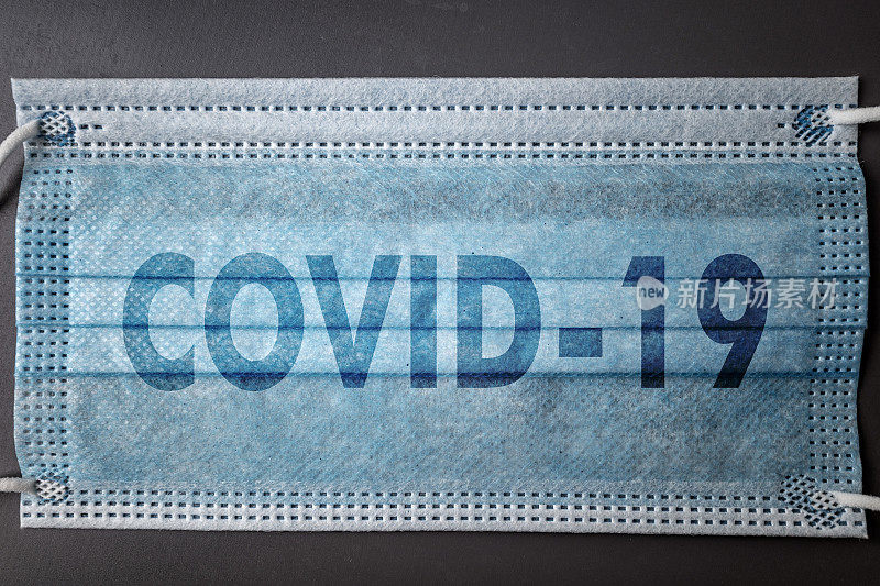 手术口罩上的Covid-19铭文，背景为深灰色