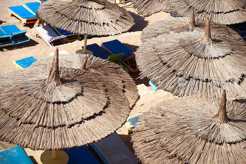 稻草沙滩伞特写抽象背景，太阳躺椅和沙子