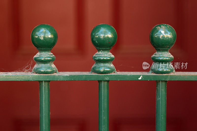 一道绿色的锻铁栅栏的一部分，靠在一扇红色的门上
