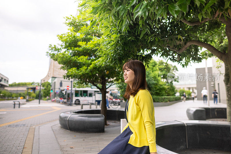 穿黄色开襟羊毛衫的日本女人正在城市里休息