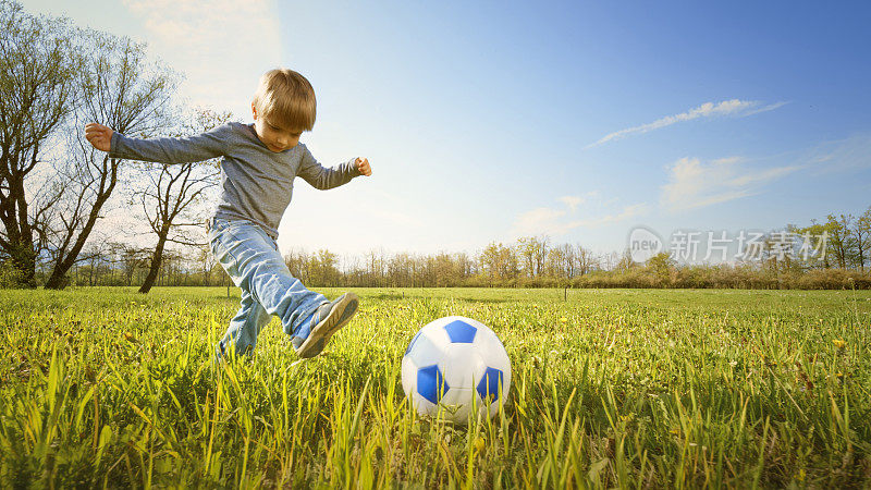 男孩在阳光明媚的草地上踢足球