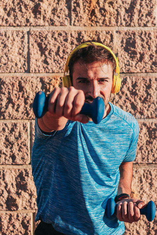 男运动员戴着黄色耳机听音乐，举重或举哑铃，在锻炼中享受乐趣。