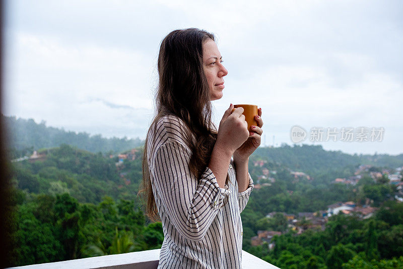 一名年轻女子在山顶上喝着茶，背景是全景