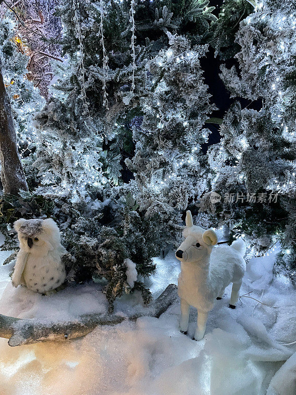 冬季林地展示的特写图像，雪花喷洒的人造圣诞树，玩具鹿和雪鸮，照亮的精灵灯