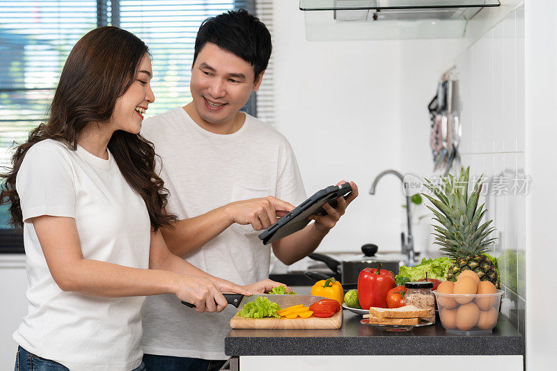夫妻俩在家里的厨房里，根据平板电脑上的食谱烹饪和准备蔬菜
