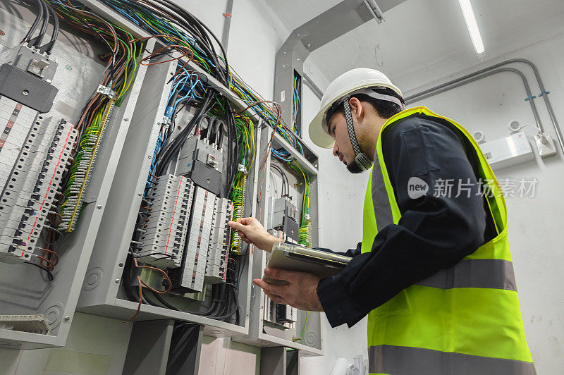 电气工程师小组工作前控制面板，电气工程师正在安装和使用平板电脑，以监测操作的一个电气控制面板在工厂服务室。