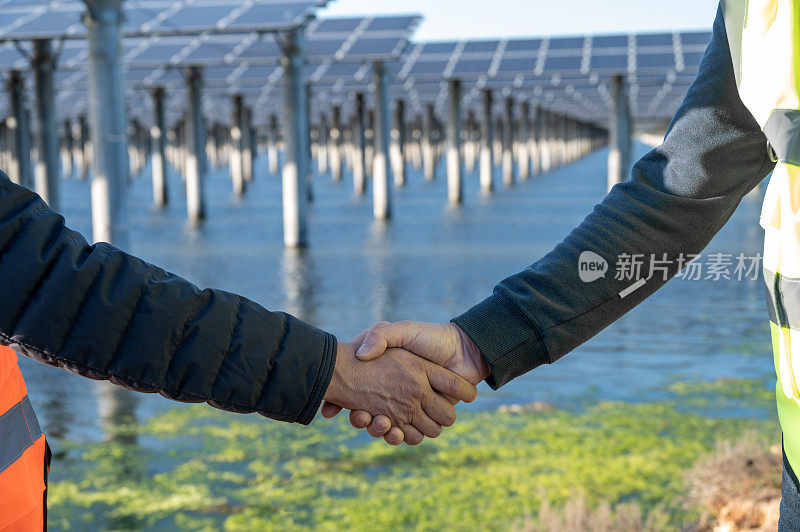 两名男工人在海边太阳能发电站前握手