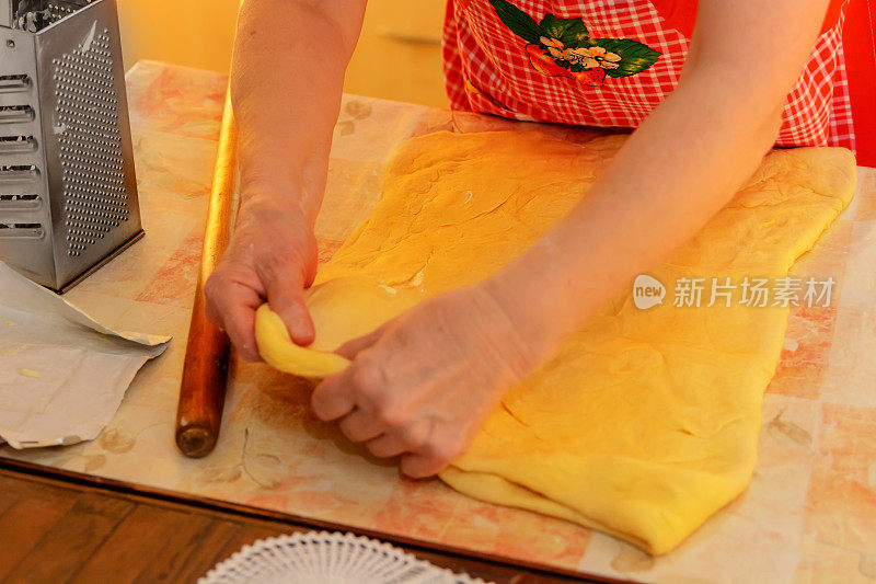 一位上了年纪的妇女正在擀面团做香肠卷。