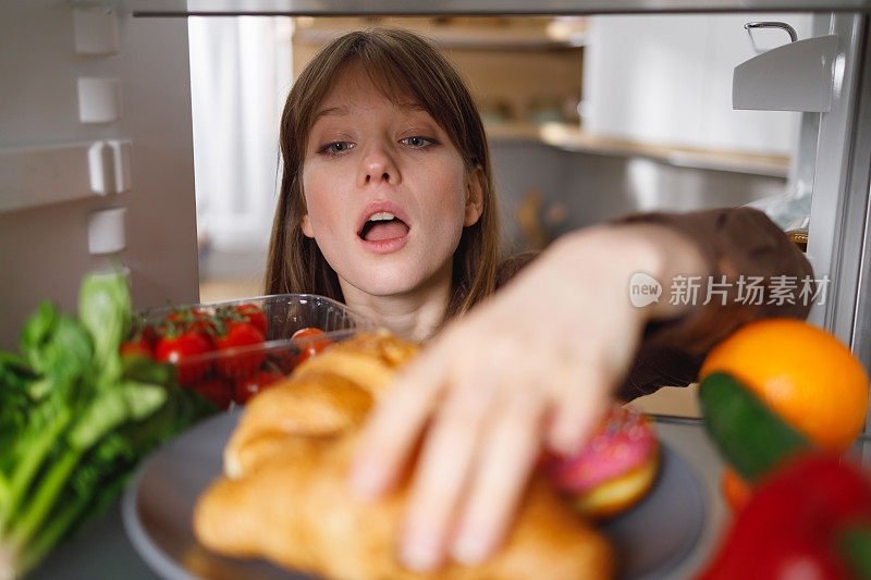 女孩从家里厨房的冰箱里拿了一个牛角面包