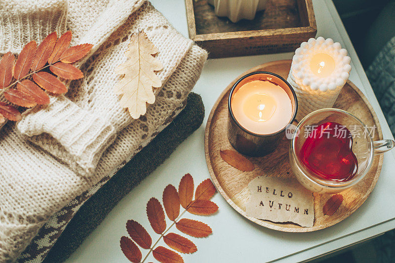 一堆针织毛衣，蜡烛，杯茶和秋叶。温馨家居室内概念，
