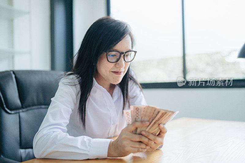 一位年轻貌美的亚洲女子穿着西装，手持泰铢钞票，货币兑换服务