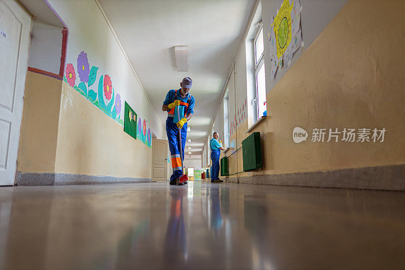 两名学校清洁工正在清理和消毒空荡荡的学校走廊