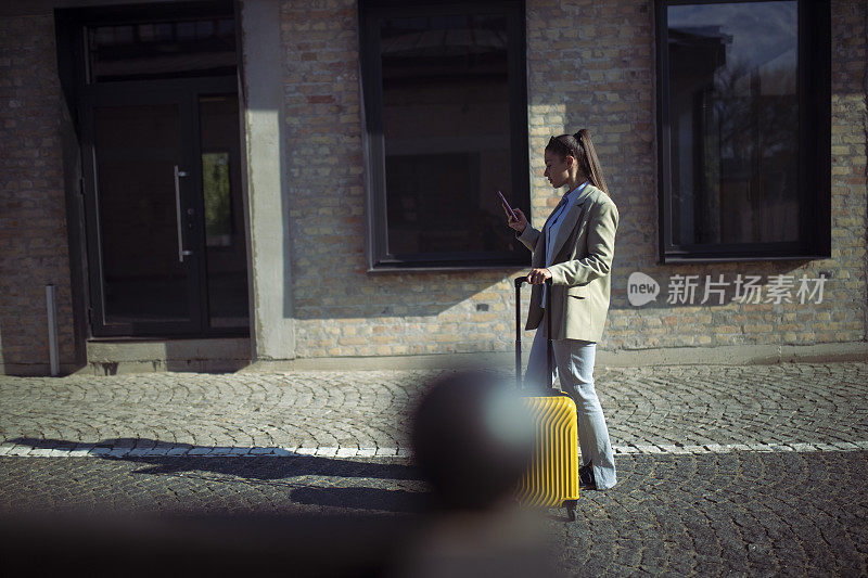 一个女人拉着行李箱走在街上，一边打着短信。