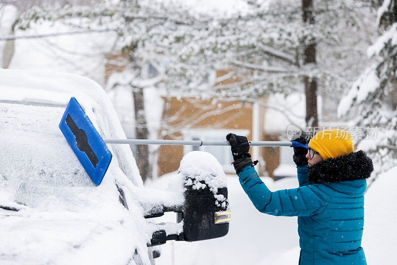 一名年轻女子在暴风雪后清理车上的积雪