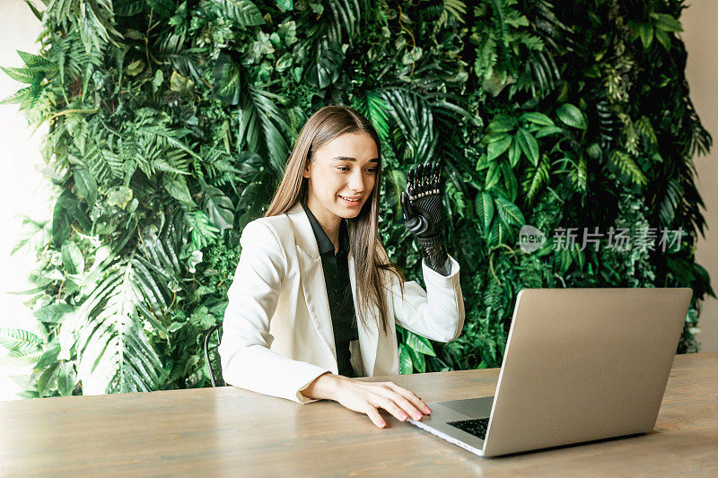一位戴着仿生假肢的年轻女子在笔记本电脑上进行视频通话。在线工作，远程学习