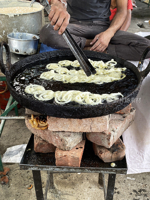 图片:贾勒比油炸面糊甜点心，户外炉子上的街头小吃，厨师用夹子搅拌金黄色的螺旋面糊，煎锅里的油沸腾，视野高远，聚焦前景