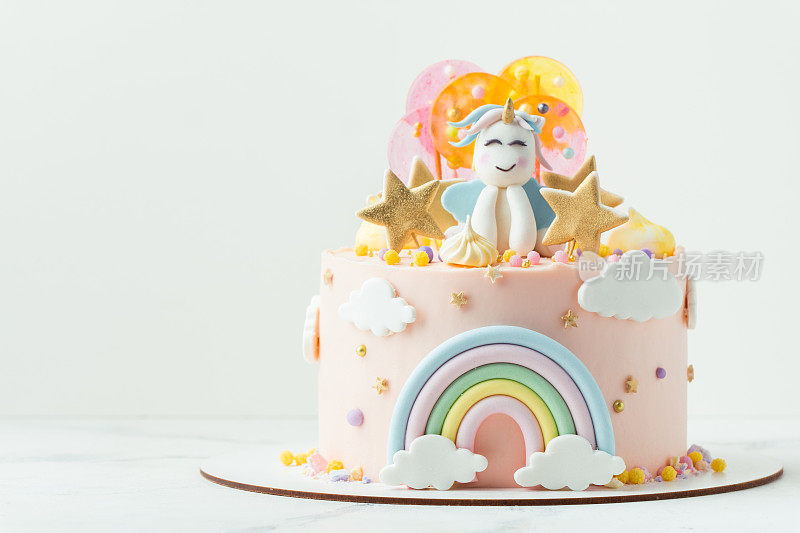 独角兽蛋糕，粉色奶油奶酪糖霜装饰乳脂彩虹，彩色焦糖糖果和独角兽形状的人在上面。白色背景上有一个小女孩的生日蛋糕