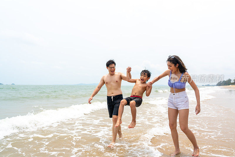 暑假，一对亚洲父母带着小儿子一起在热带海滩上玩海。