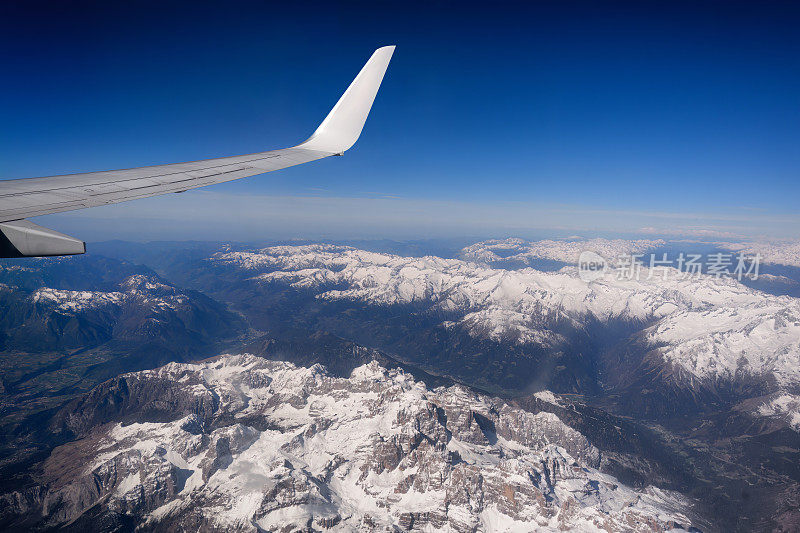 飞越瑞士阿尔卑斯山的雪山，看到飞机的机翼。乘飞机旅行。