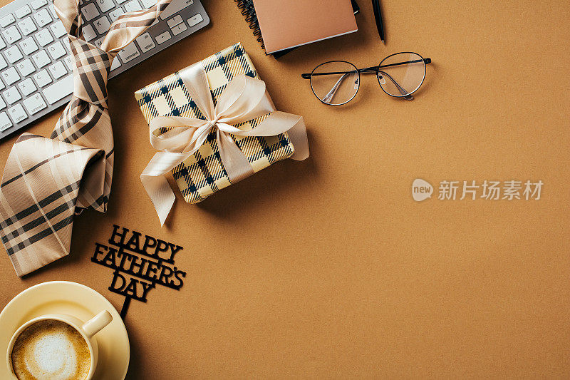 父亲节快乐的概念。办公室桌子上有礼盒、眼镜、键盘、领带、咖啡色背景的咖啡杯。