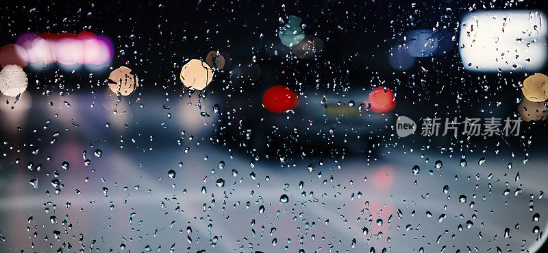 雨点落在汽车挡风玻璃或车窗上，背景是模糊的道路。雨季开车。雨滴落在汽车后视镜上。傍晚有雨的交通道路。毛毛雨会降低行车能见度