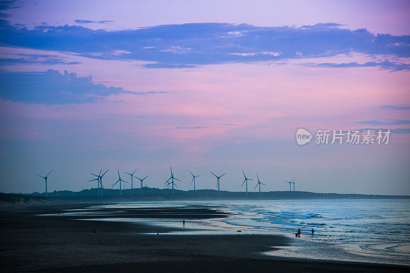风力涡轮机的风扇在波光粼粼的海面上旋转。日落时的动态云。