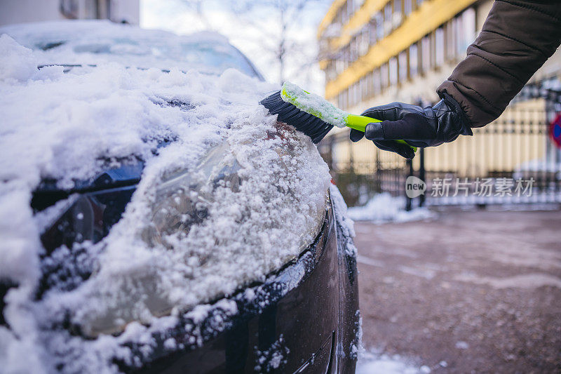 年轻人正在清除汽车前灯上的雪