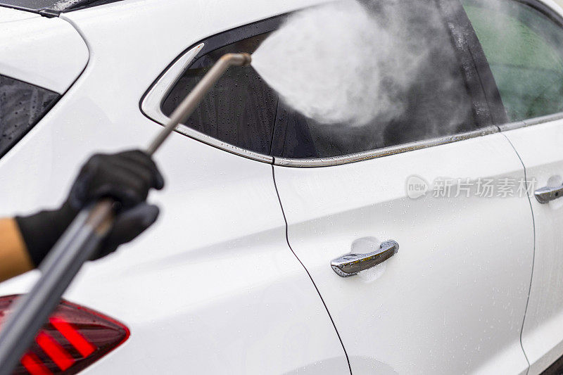 一名男子用加压软管里的水冲洗汽车上的泡沫，这是一家自助洗车店