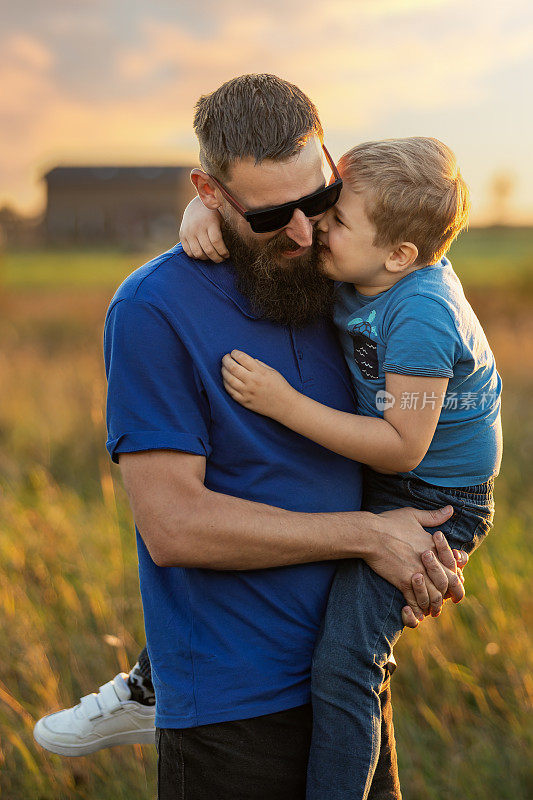 儿子和父亲之间强烈的拥抱。父子情谊。朦胧的乡村田野被金色的夕阳照亮。