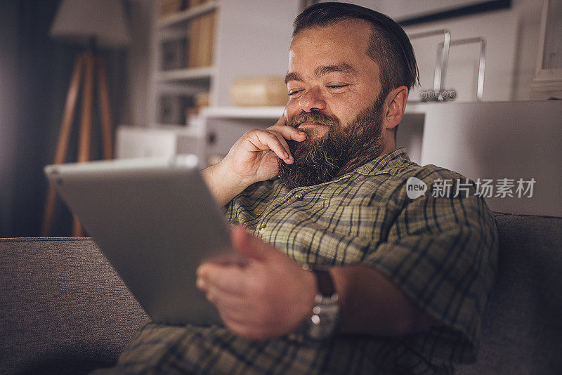 在家沙发上玩平板电脑的快乐男人