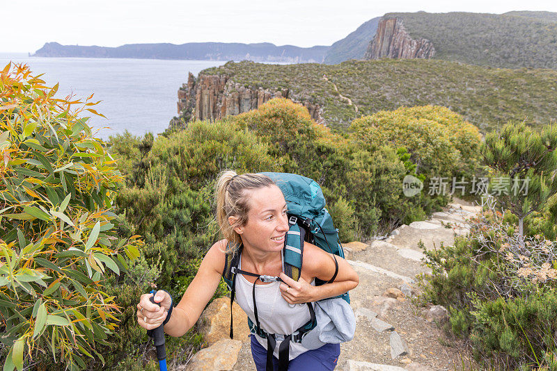 “孤独的脚步:一位女性徒步旅行者在塔斯马尼亚半岛小径上的宁静漫步，周围是悬崖边的威严”