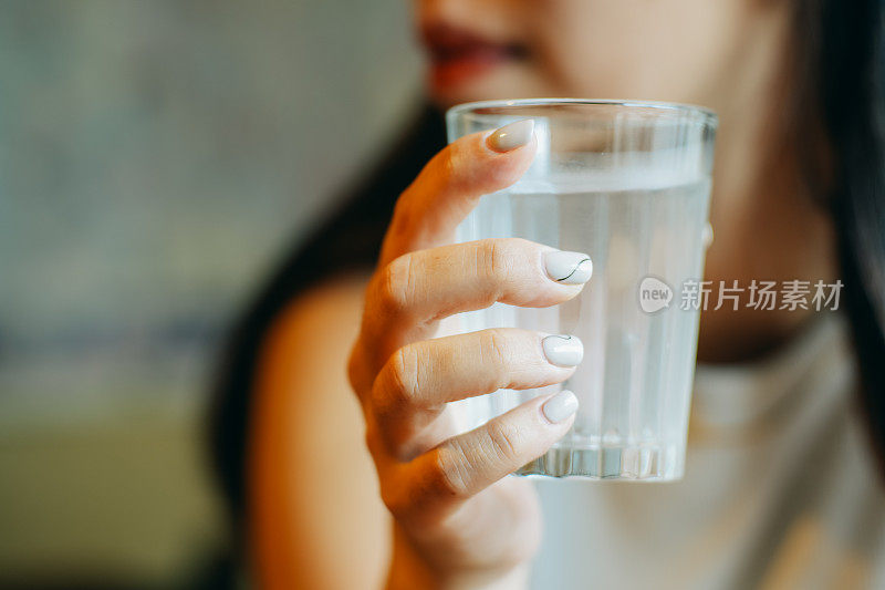 这张照片描绘了一个宁静的时刻，一个女人拿着一杯透明的纯净水。她精致的指甲与清澈的水面形成对比，在模糊的背景中营造出一种平静和安宁的感觉。