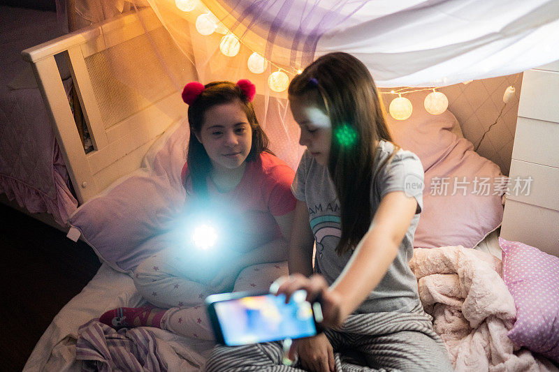 姐妹们自拍或用智能手机在家里舒适的灯光小屋拍摄-有特殊需要的女孩