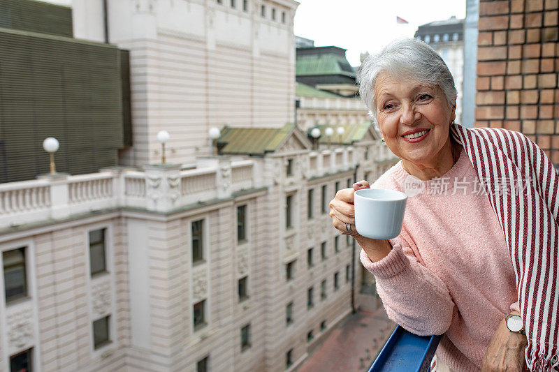 老妇人在阳台上喝着咖啡，享受着白天的时光