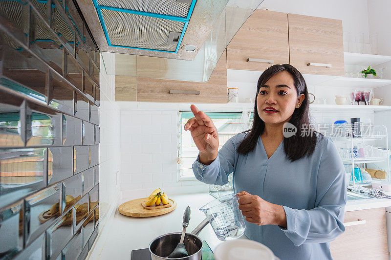 亚洲成熟女性在厨房准备和烹饪健康的食物，男人在家里使用智能表面或UX界面(空白表面墙)，智能未来的家庭和物联网概念