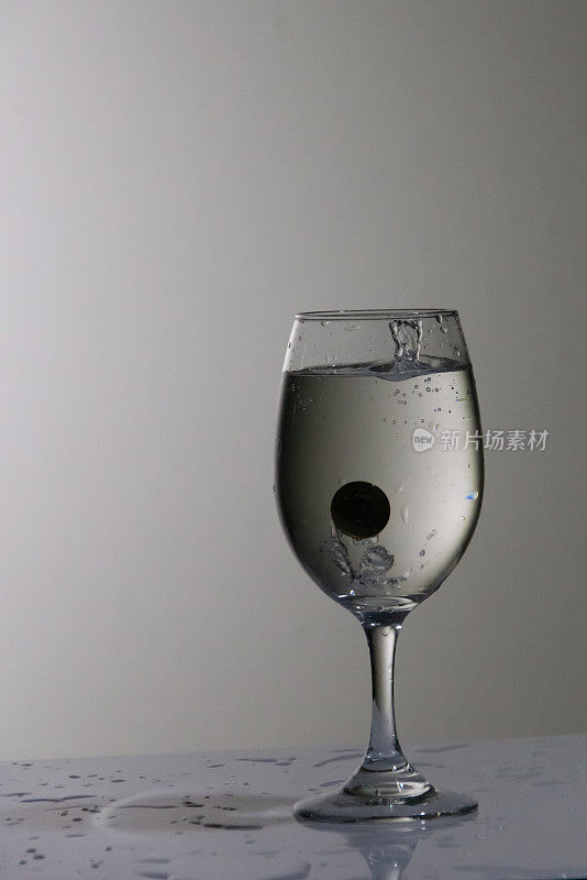 硬币掉进一个盛满水的玻璃杯里，放在一张白色背景的桌子上