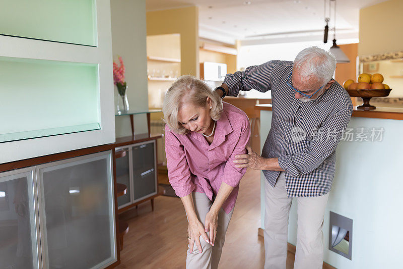 一位老年妇女在家里膝盖有问题，但她的丈夫正在帮助她减轻疼痛。