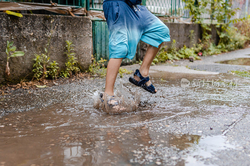 小男孩在泥坑里溅起水花，跳进水坑里