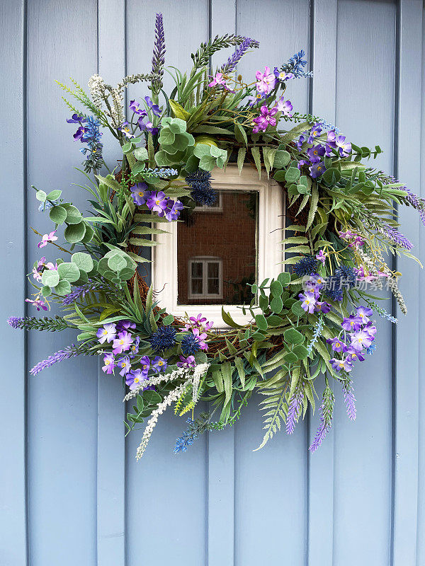 淡蓝的特写图像，木制镶板前门与眺望窗外和夏季花环装饰紫色，丝绸花和塑料，绿色树叶