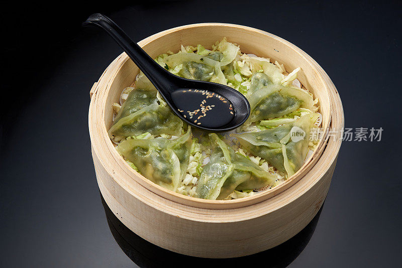 亚洲美食:在双层竹制蒸锅里，加入菠菜和奶酪的饺子，深色背景上放着酱油