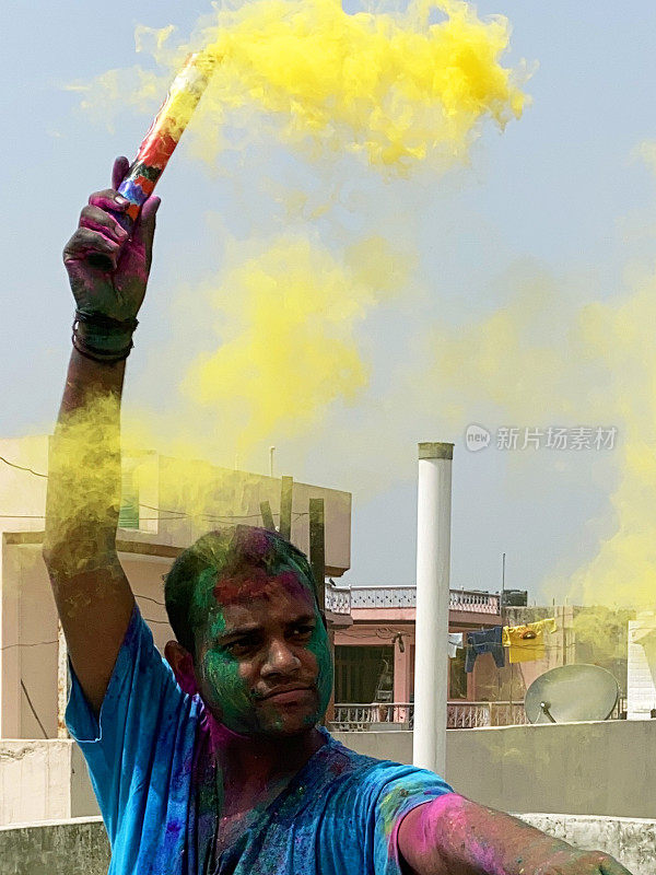 一名印度教徒站在屋顶上，身上涂满了漆粉，他释放了一枚黄色烟雾弹，在胡里节的色彩和爱漆大战中胡闹
