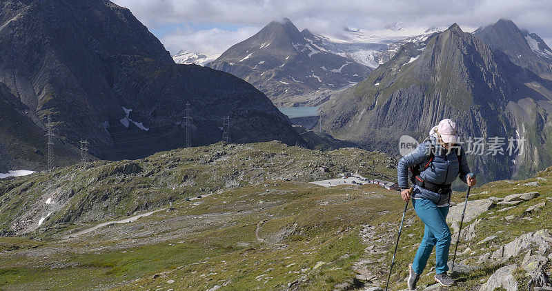 一名女性徒步旅行者在冰川覆盖的山脉和池塘上方攀登高山