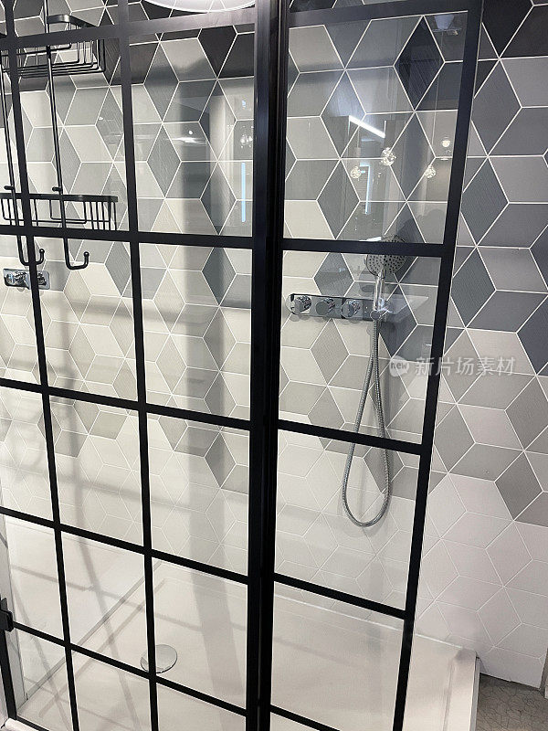 现代浴室的形象，独立的淋浴间后面的镶板玻璃门，灰色，黑白几何墙砖立方图案设计，当代铬淋浴挂在墙上，搅拌机龙头，肥皂篮