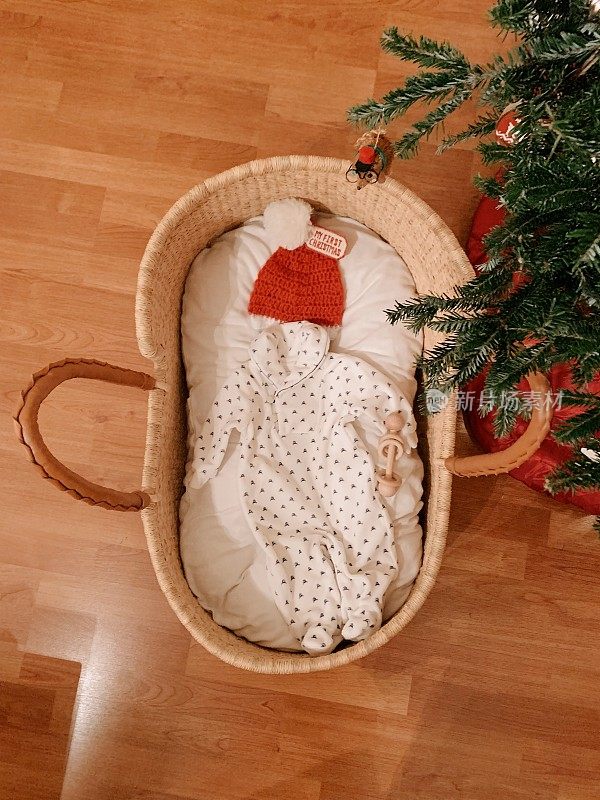 手工制作的摩西篮子放在一棵真正的圣诞树下，圣诞树上装满了婴儿物品，等待着一个圣诞男婴