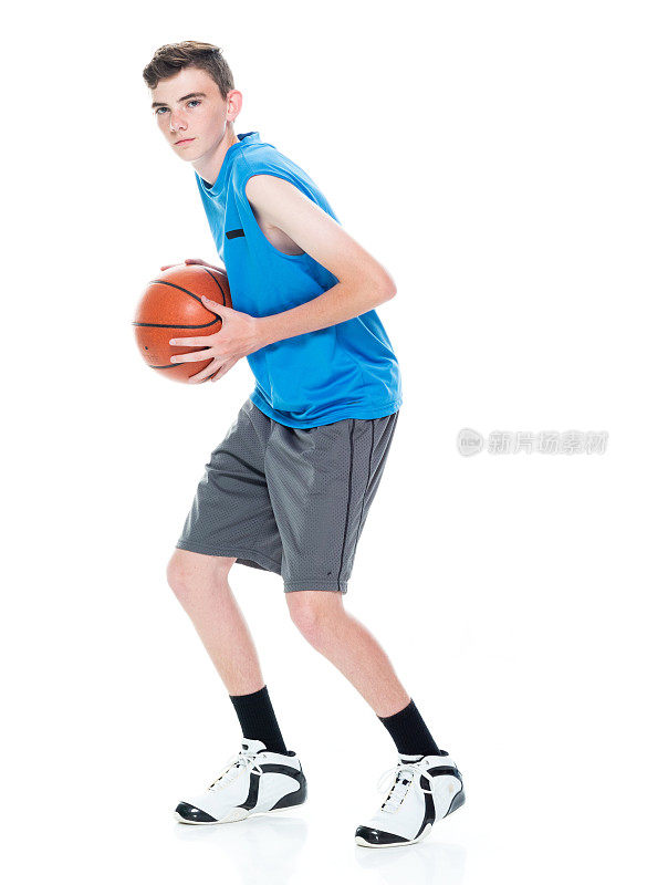 白人少年篮球运动员站在白人背景前，手持篮球和使用运动球