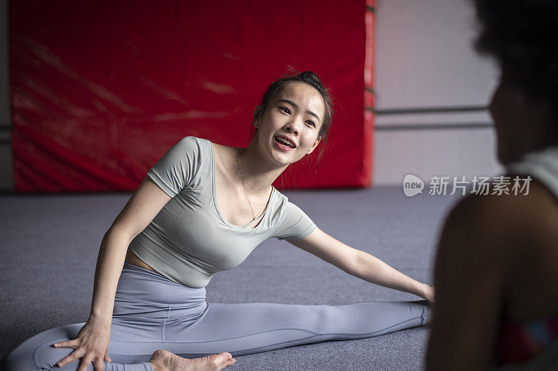 亚裔中国女人在健身房伸展时微笑和聊天的中景