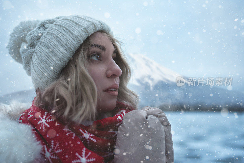 滑雪胜地迷人女子的肖像站在结冰的湖岸边，雪花落在她的脸上，冷风吹过，她微笑着。