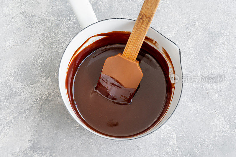 融化的黑巧克力滴和黄油在白色平底锅里放在桌子上。制作釉彩、巧克力蛋糕、熔岩蛋糕、布朗尼的过程。前视图。